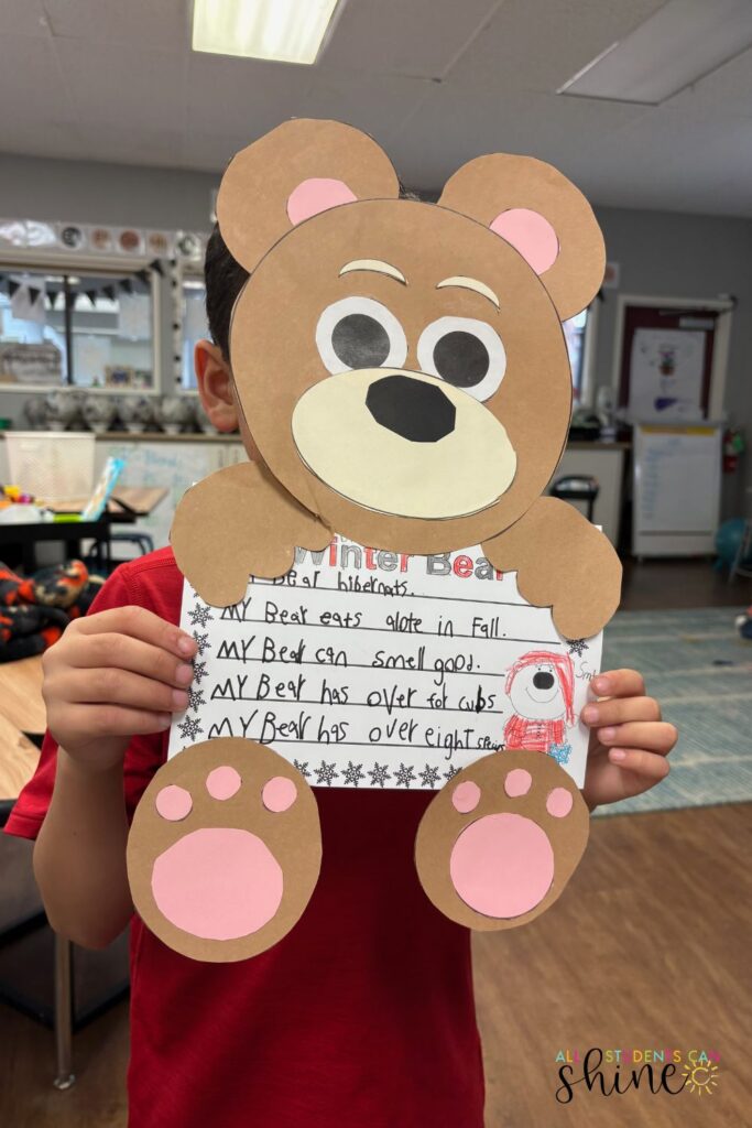 A student holding a completed Winter Bear craftivity featuring a large paper bear with pink paws and a writing prompt about bears. The craftivity includes fun facts about bears and a small drawing of a bear in a winter hat. This winter craftivity blends creativity with writing practice, making it a fun seasonal classroom activity.