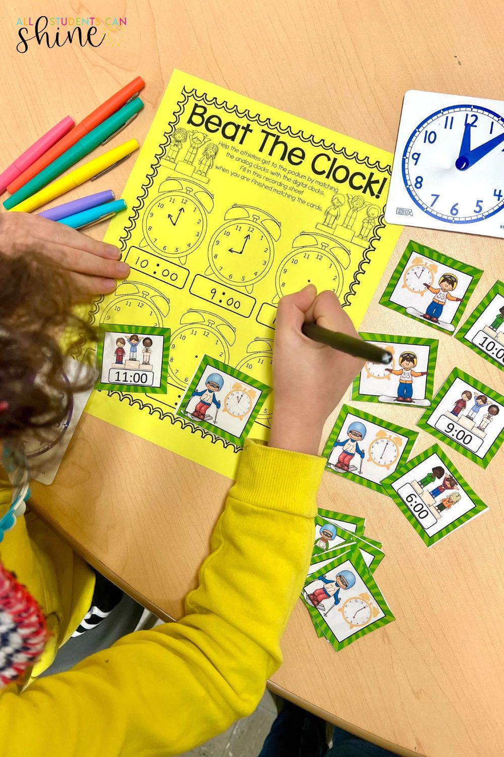 Winter sports-themed telling time activity for elementary students. A child wearing a yellow sweater completes a 'Beat The Clock!' worksheet, matching analog clocks to digital times. The table includes colorful markers, a small teaching clock, and time-matching cards featuring winter athletes. A fun hands-on math center for time-telling practice.