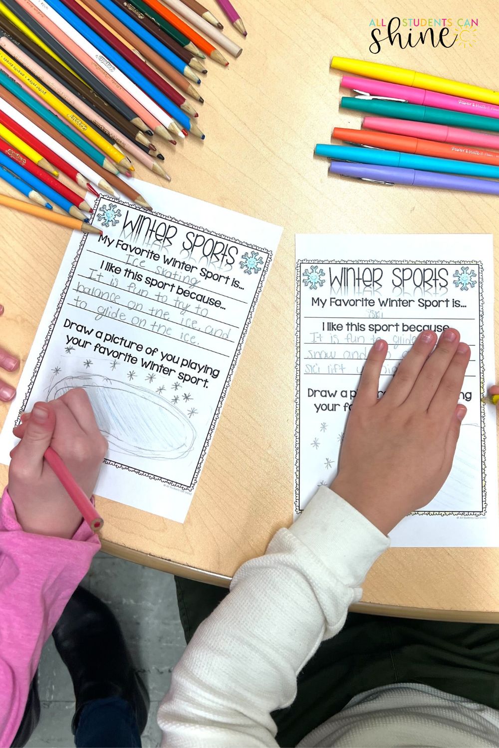 Winter sports writing activity for elementary students. Two children work on worksheets titled 'Winter Sports,' writing about their favorite winter activity and drawing a related picture. The table is filled with colorful pencils and markers, creating an engaging classroom environment for literacy and creativity.